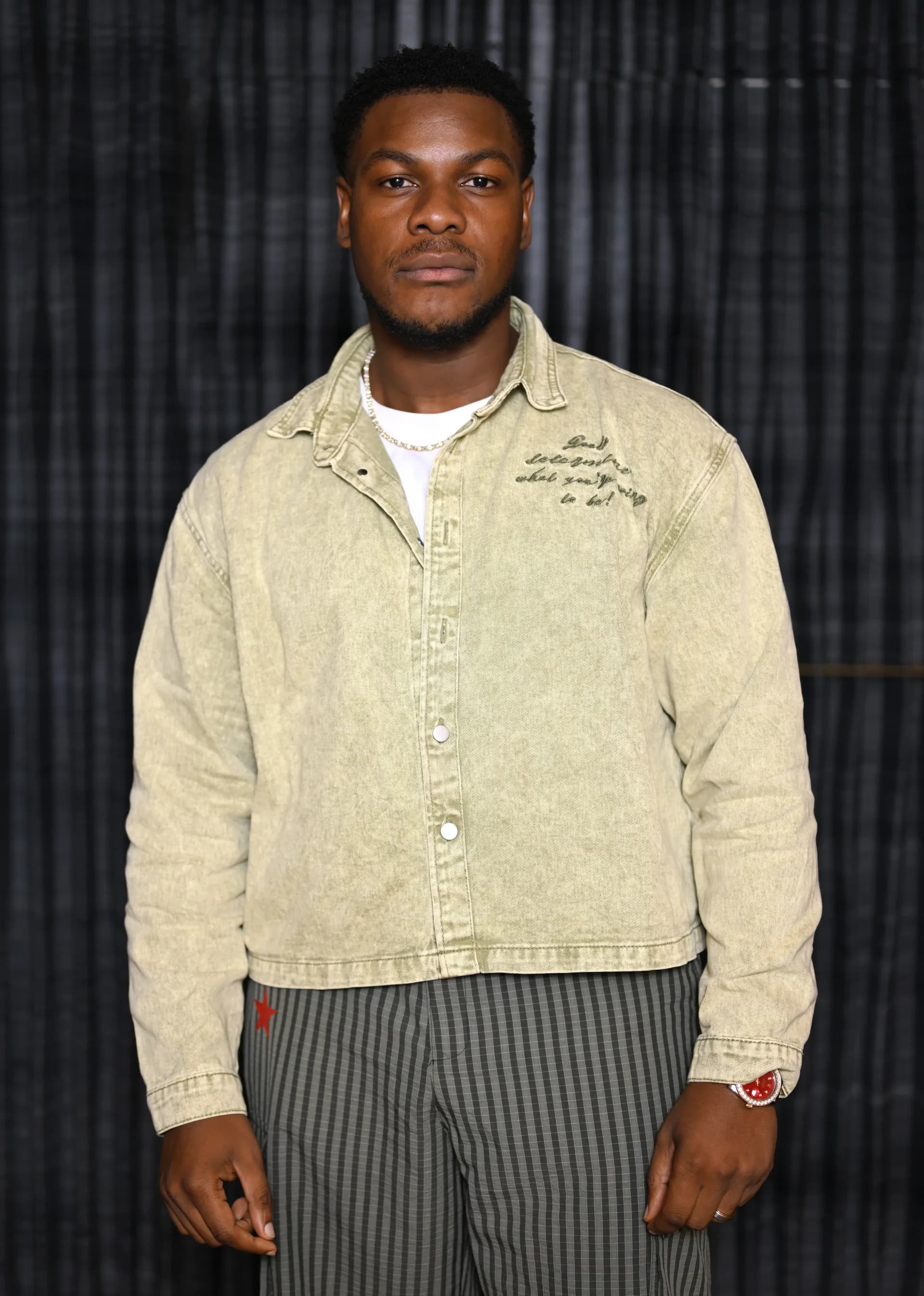 John Boyega smiling in a suit, wearing a simple silver band on his left hand.