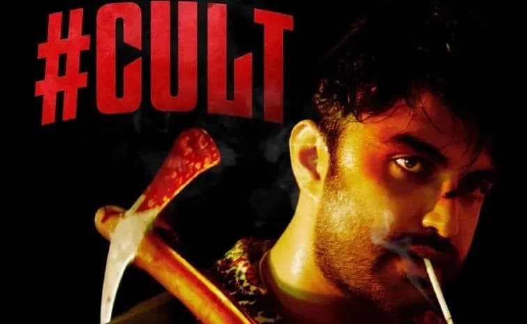 A still from the film 'Cult' showing Vishwak Sen in a tense scene, wearing a mask, standing in a dimly lit forest.