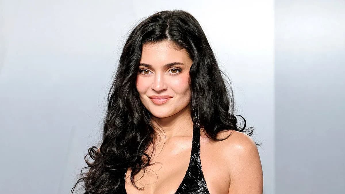 Kylie Jenner in a dramatic pose, standing near a pool, wearing a white dress, with a tense expression.