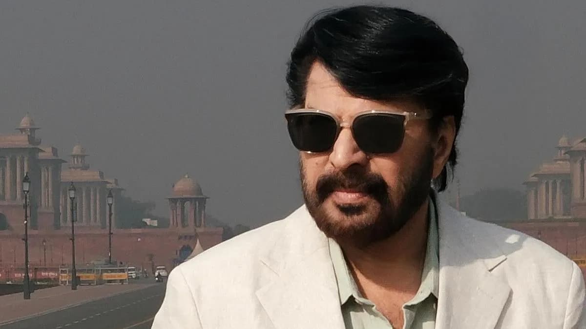 A black-and-white still of Mammootty as Sethurama Iyer, standing in front of a police station, hands behind his back, staring ahead.