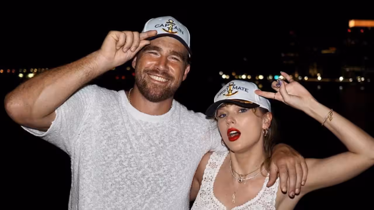 Taylor Swift in a black strapless midi dress holding hands with Travis Kelce in an olive green shirt and shorts outside a restaurant at night.