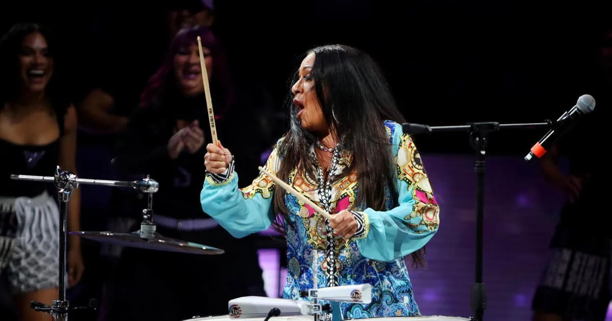 Sheila E. speaking into a microphone, looking distressed, during a post-festival interview.