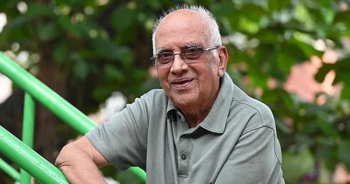 A black-and-white photo of Singeetham Srinivasa Rao in his late 80s, wearing a white kurta, holding a script, eyes sharp with focus.