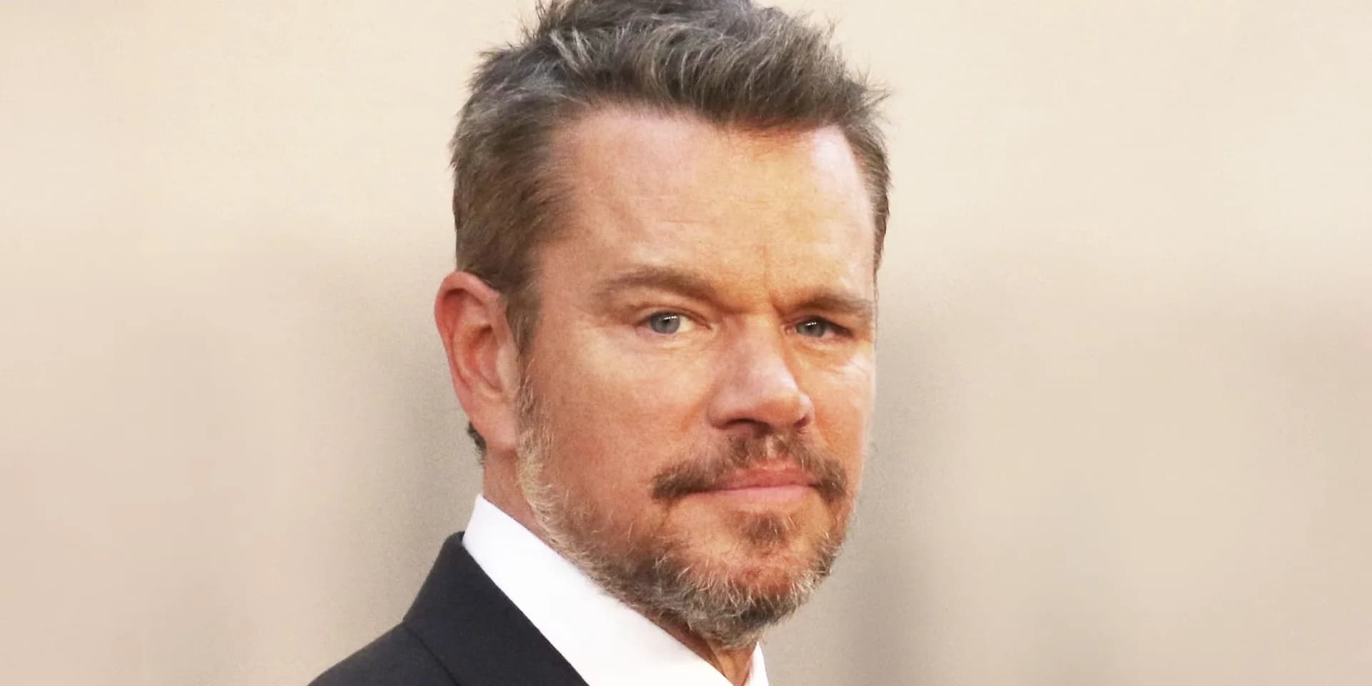 Matt Damon as Tom Ripley in a suit, standing in front of a window, looking out with a calm expression.