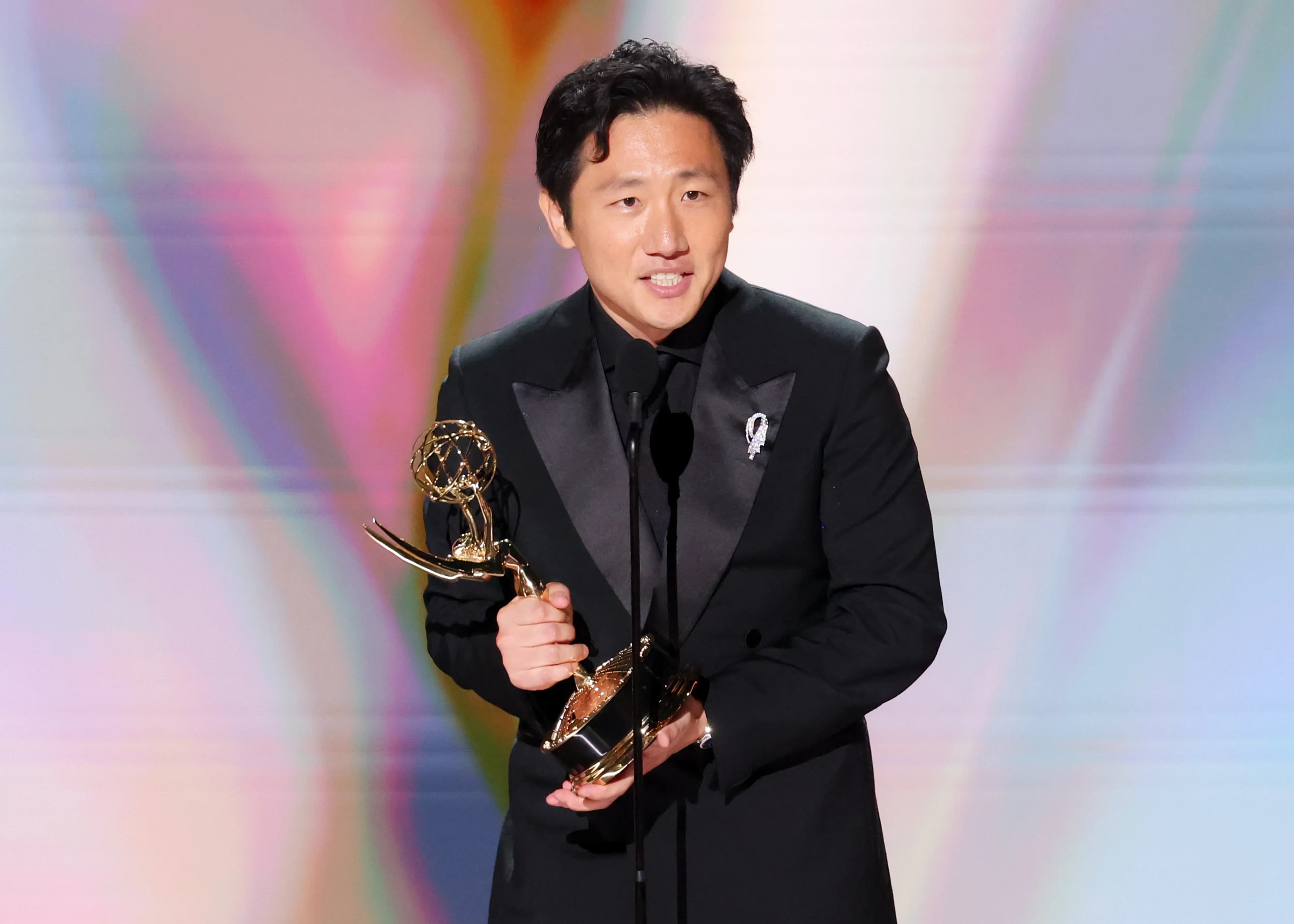 Hiro Murai holding his Emmy statuette on stage after winning Outstanding Directing for a Comedy Series for Widow's Bay.