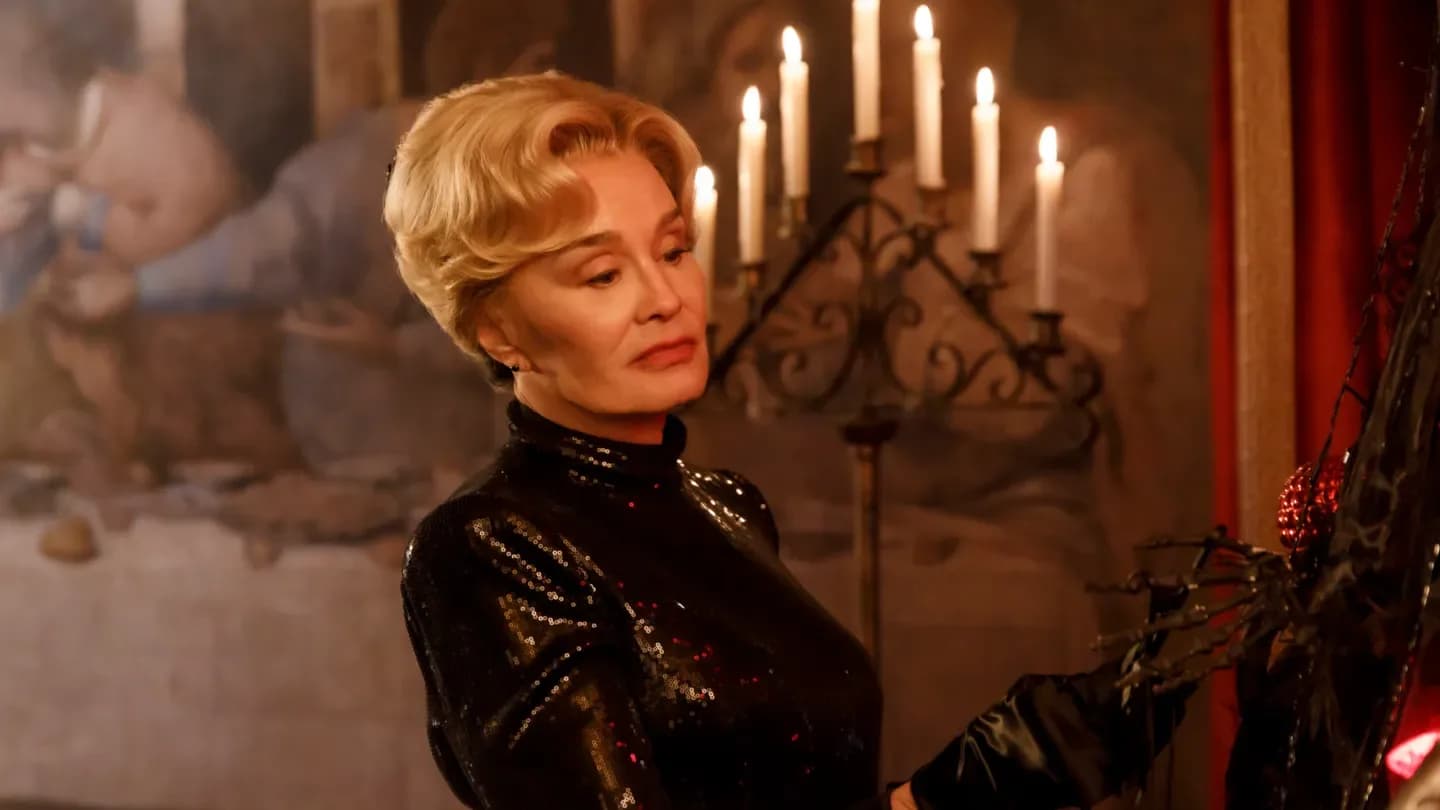 Jessica Lange in a dramatic red dress, standing in front of a haunted house.