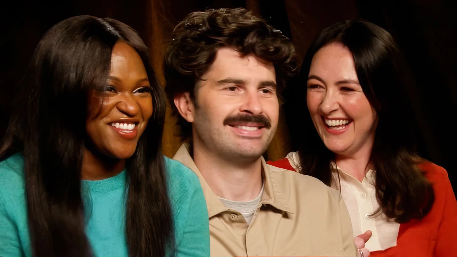 Emma Sidi, Ayoade Bamgboye and Paddy Young standing together on the SNL UK set, smiling in front of a backdrop of sketch props.