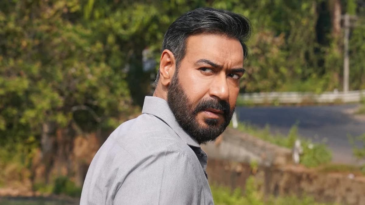 Ajay Devgn in a tense scene from Drishyam 3, standing against a dark backdrop.