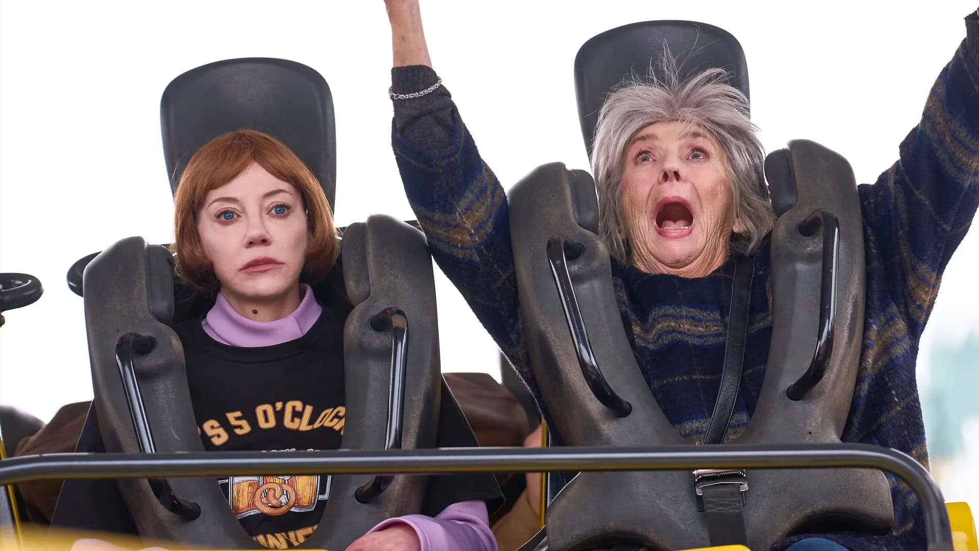 Sue Johnston and Diane Morgan in a quiet moment on a couch, surrounded by cluttered household items. The robot’s face is slightly glitching, the human’s eyes are tired but warm.