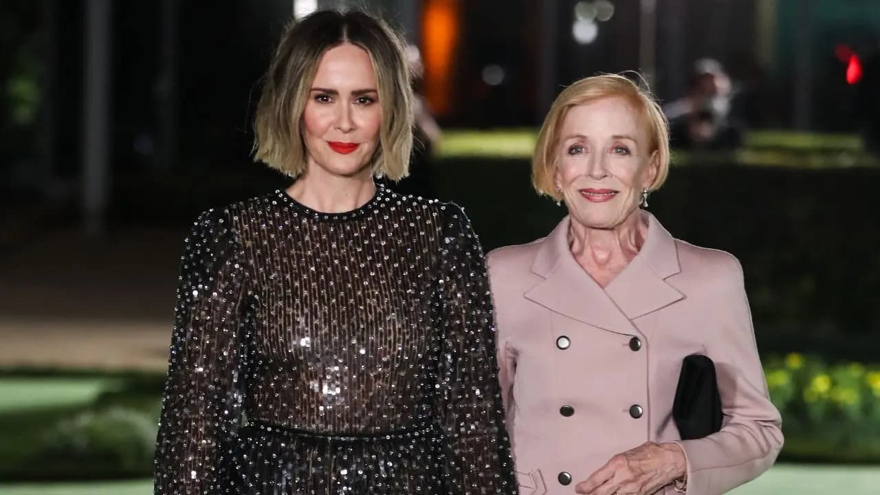 Sarah Paulson and Holland Taylor hold hands while posing together on the red carpet in black outfits.