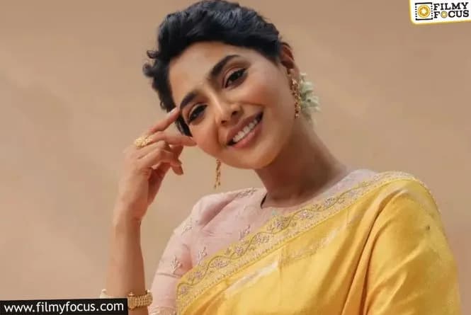 Aishwarya Lekshmi smiling at a press event, holding a microphone.