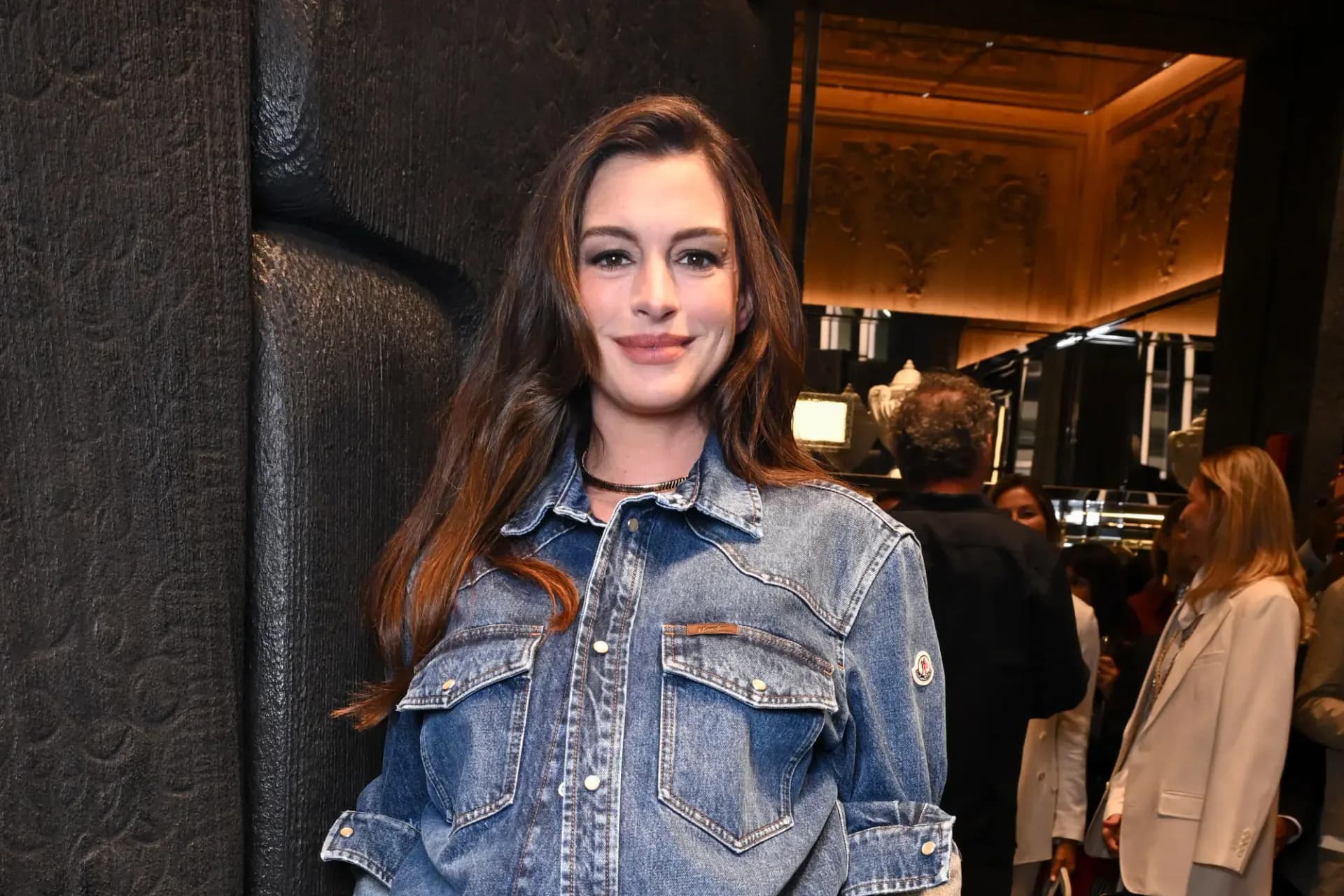 Anne Hathaway in a Verity promotional still, holding a microphone with a blurred plate of chicken wings in the background