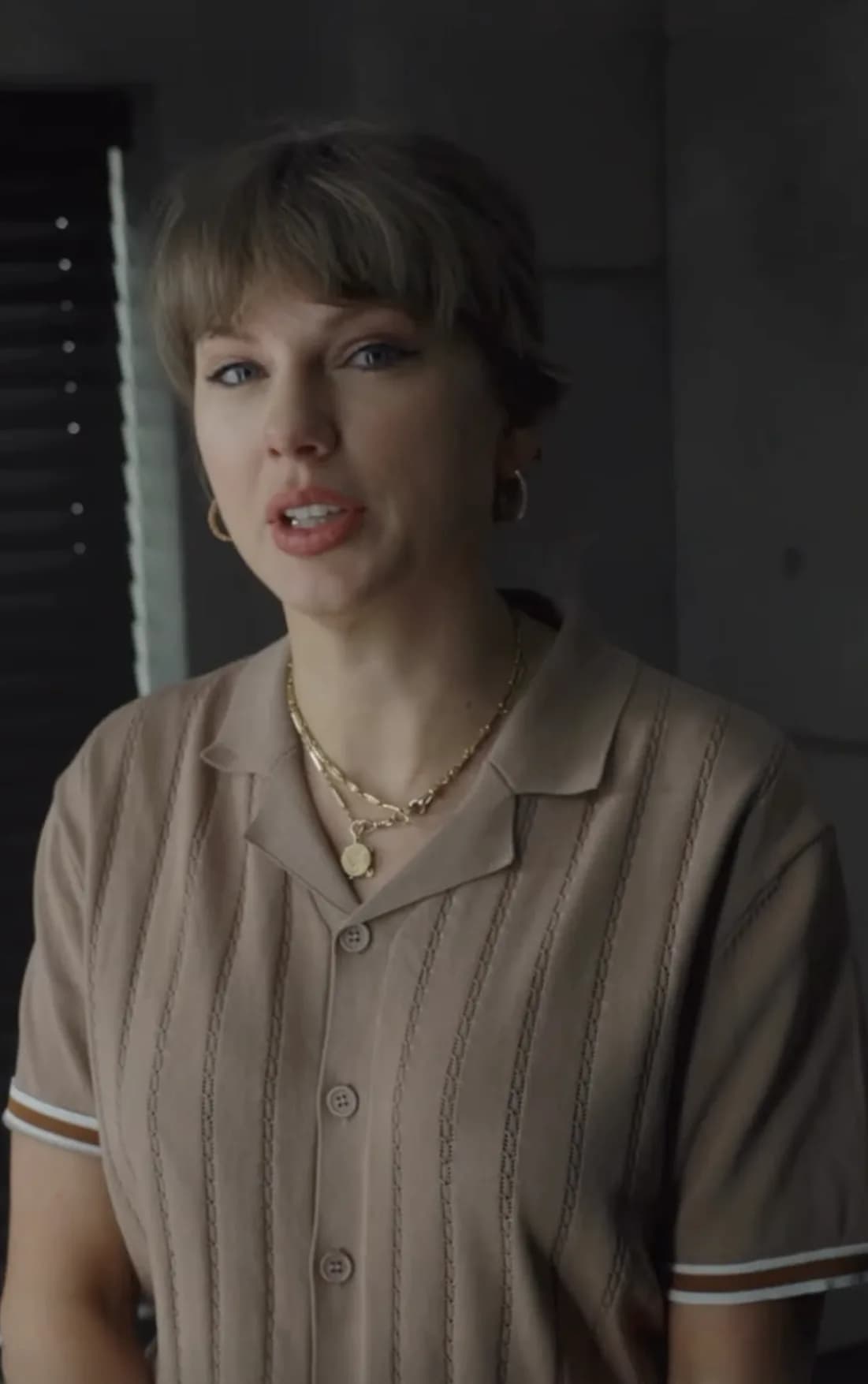 Taylor Swift wearing camel-colored polo shirt in ‘Patient Zero’ teaser, gold jewelry visible