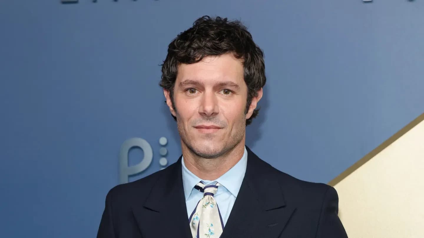 Adam Brody at a media event, smiling in a dark suit