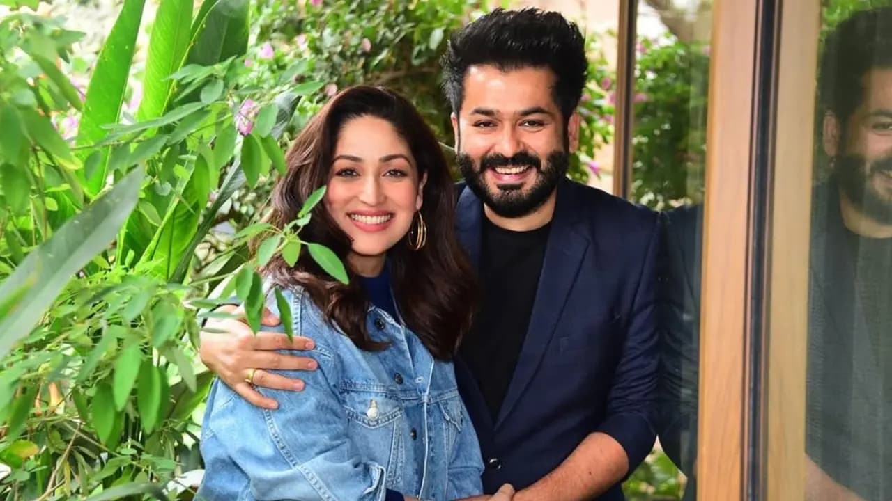 Yami Gautam at a promotional event, smiling at the camera, holding a phone with a photo of Aditya Dhar.
