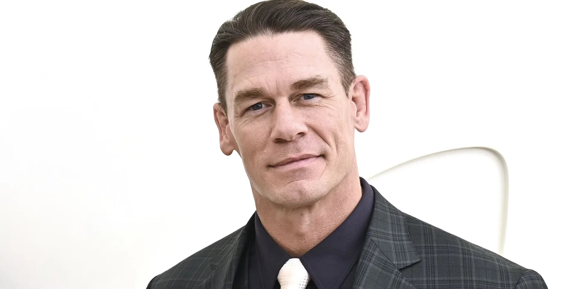 John Cena in a tactical jacket, standing in front of a car, mid-action pose.