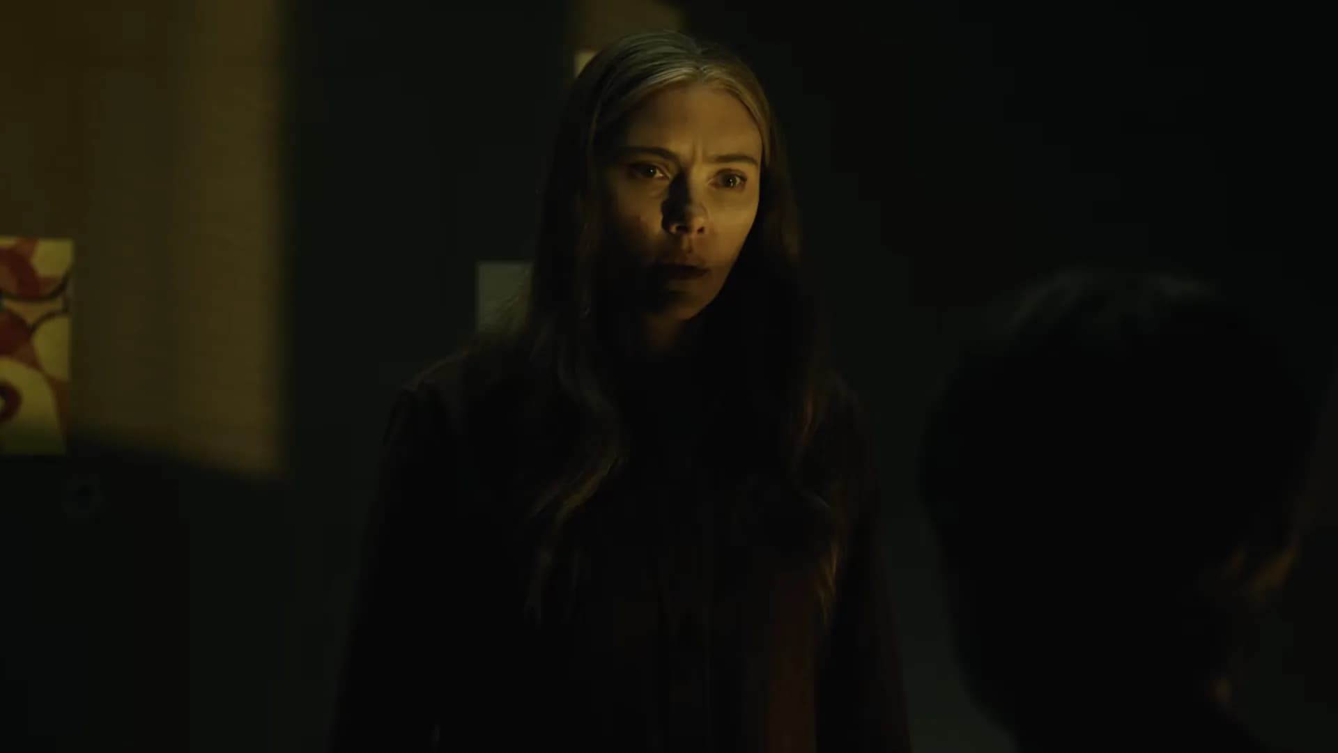 Scarlett Johansson in a dimly lit church, staring at blood-written words on stone walls.