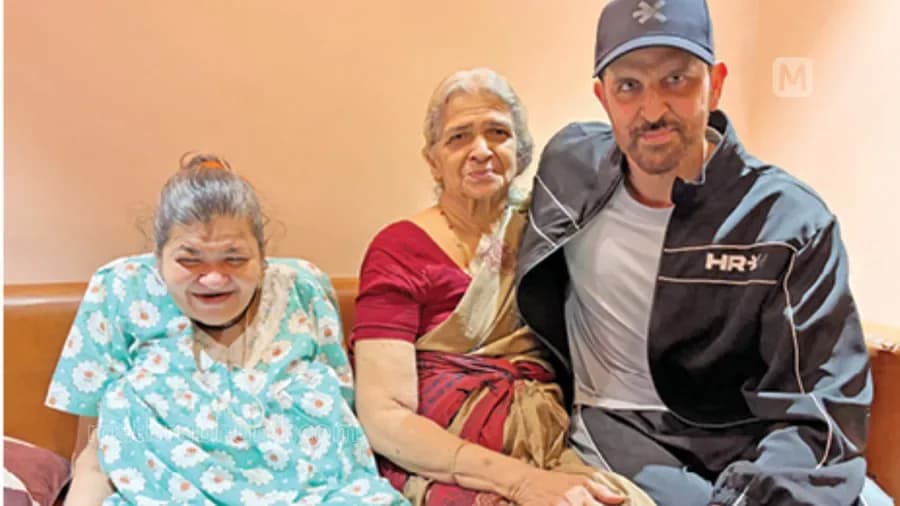 A woman with cerebral palsy sits in a wheelchair, smiling beside Hrithik Roshan in a Mumbai meeting room. Both are dressed casually, faces lit with warmth.