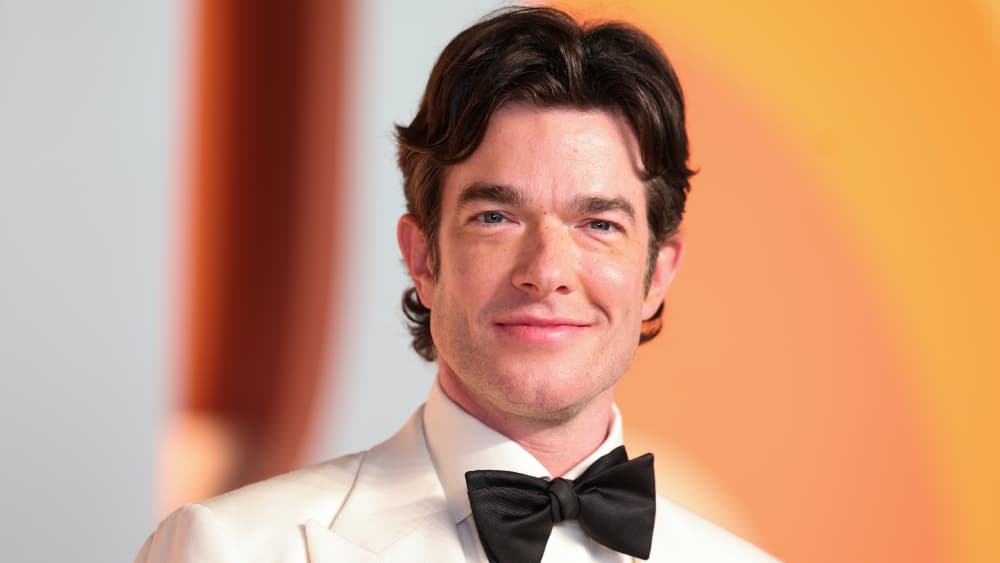 John Mulaney at a public appearance, smiling in a suit.