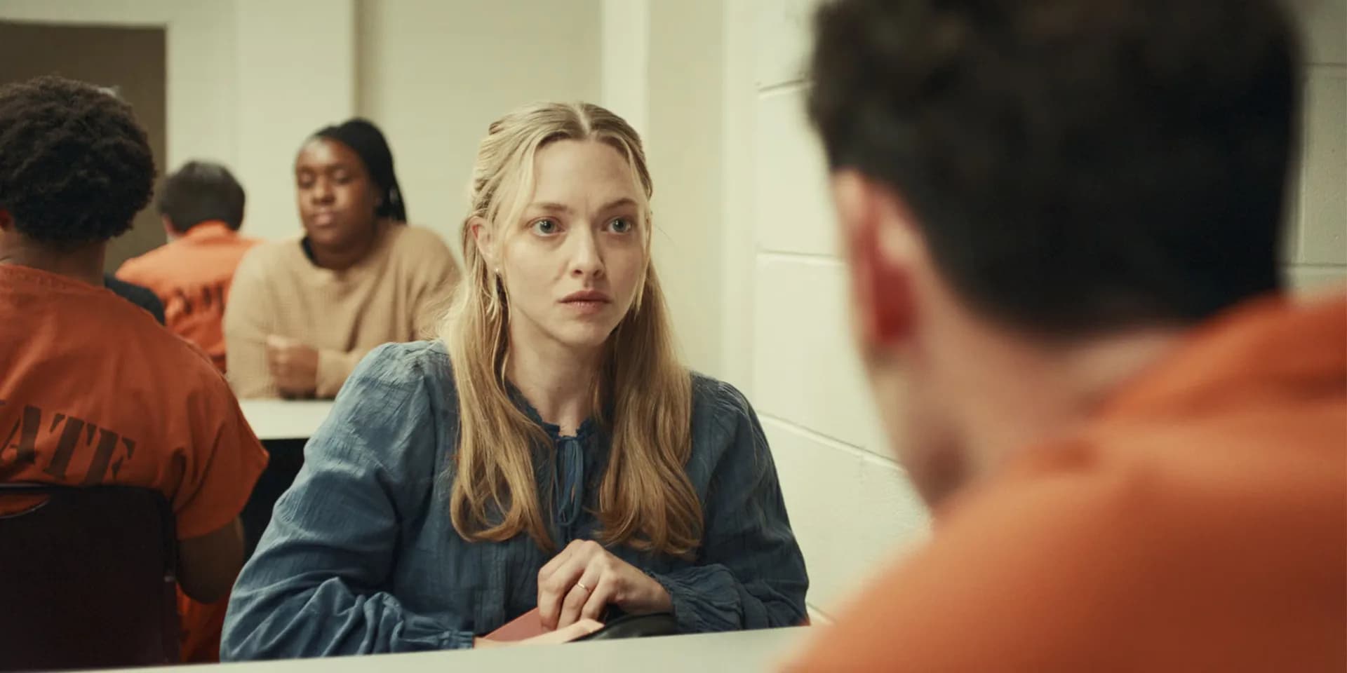 A still from The Life and Deaths of Wilson Shedd showing Amanda Seyfried and Scoot McNairy in a dimly lit prison setting.