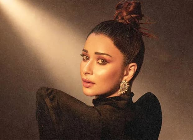 Nyrraa M Banerji in a soft-lit studio, eyes closed, singing into a mic.