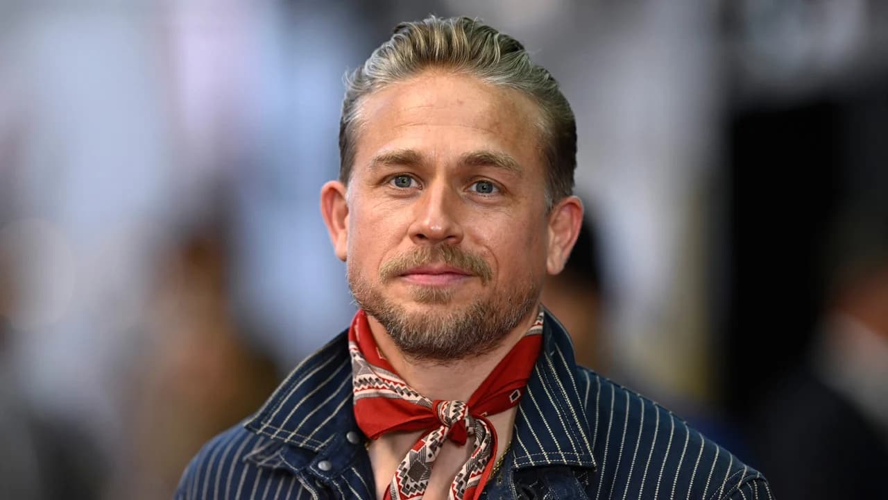 Charlie Hunnam at a press event in a dark blazer, smiling for photographers.