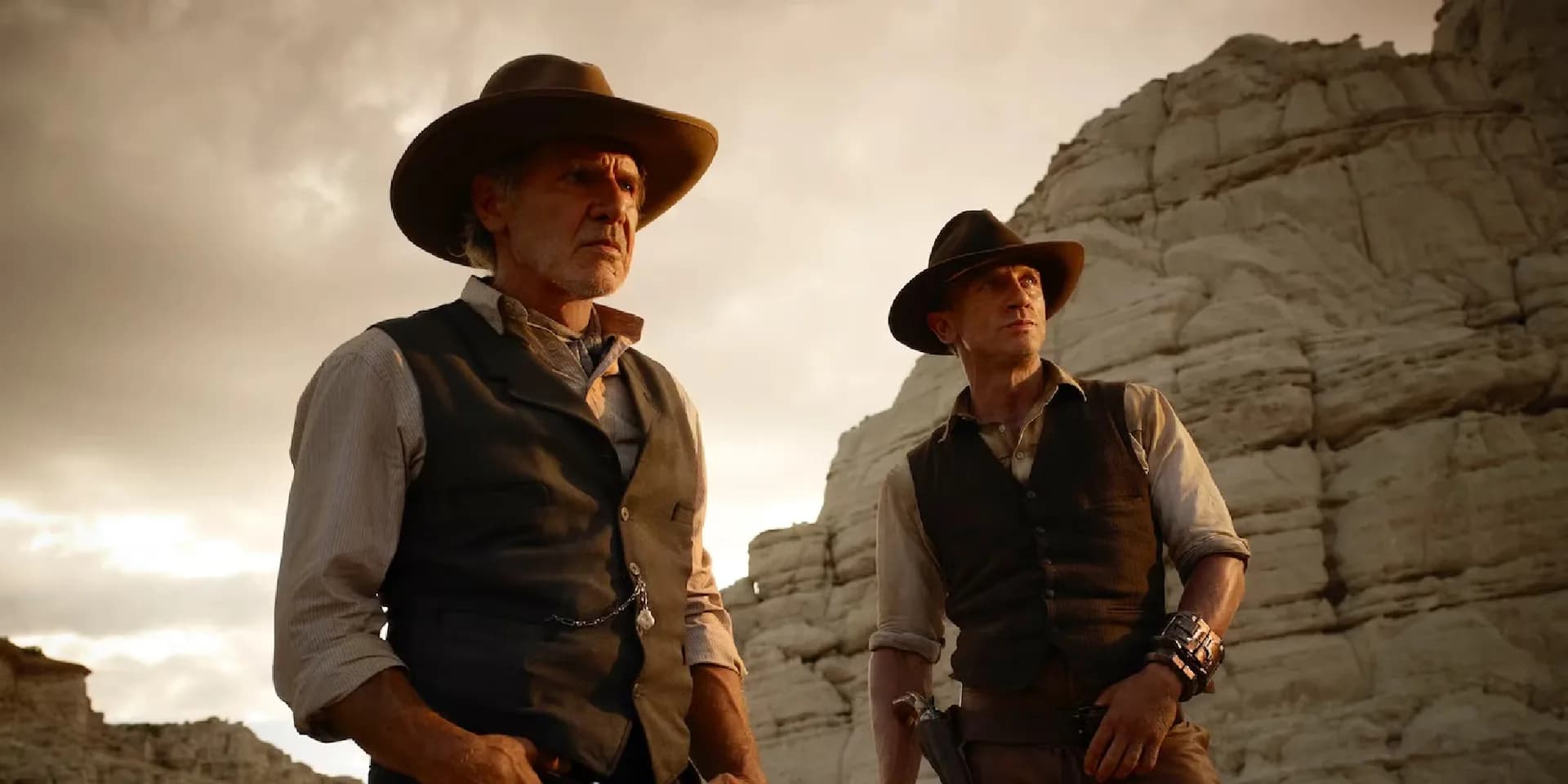 Daniel Craig and Harrison Ford in a dusty Western scene, surrounded by alien ships and smoke.