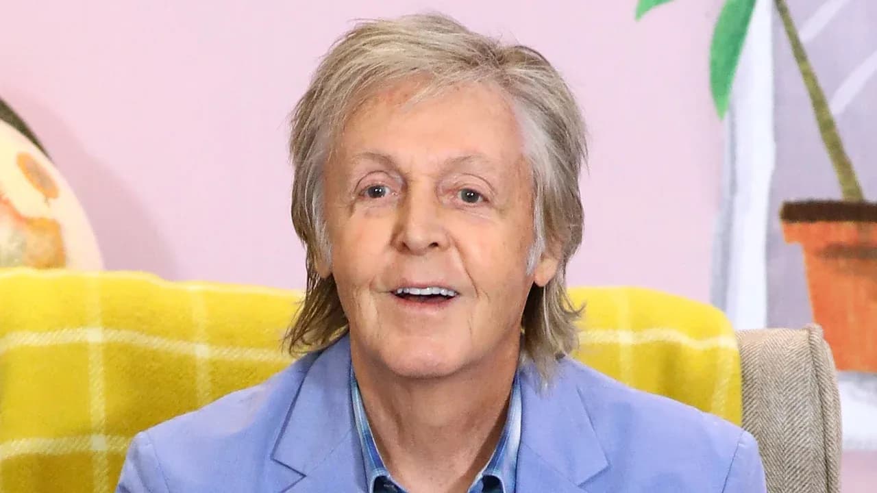 Paul McCartney performing on stage, smiling at the camera.