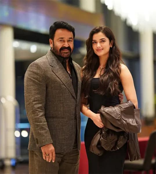 Bhagyashri Borse and Mohanlal standing together, smiling, with a city skyline behind them