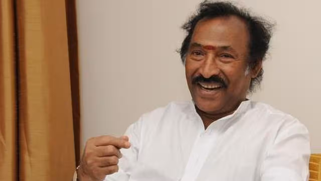 Portrait of music composer Deva in profile, mid-speech, holding a microphone.