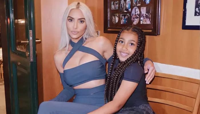 A candid shot of Kim Kardashian and North West laughing together during a family outing, sunlight catching the edges of their faces.