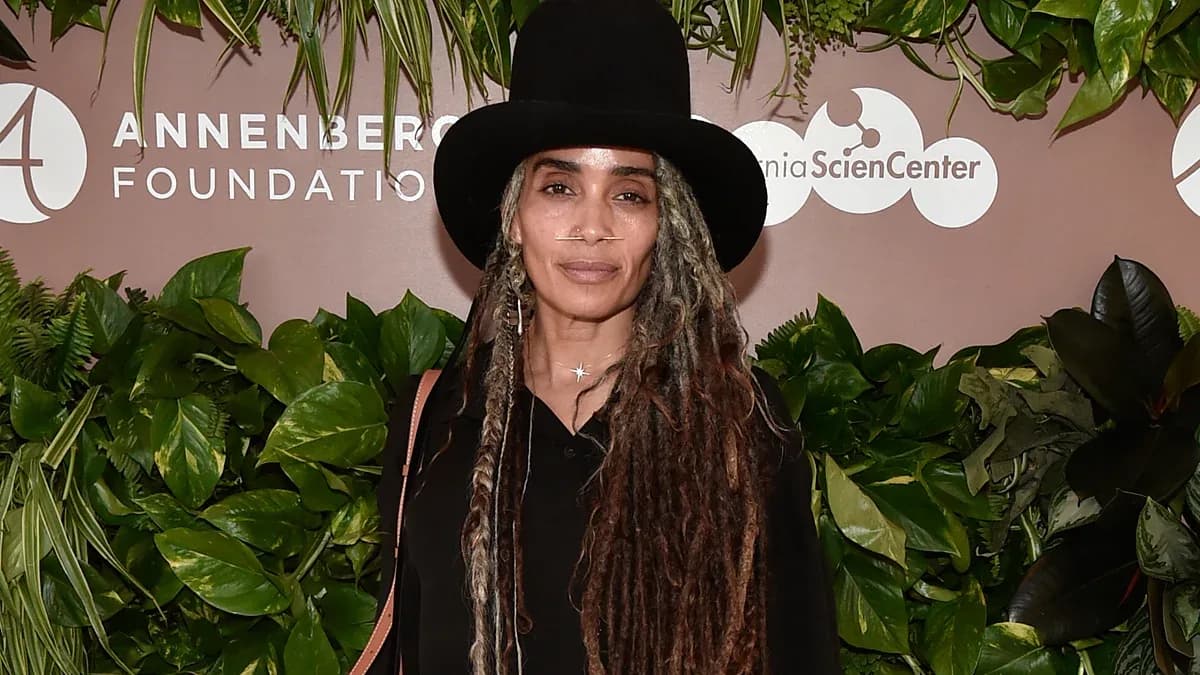 Lisa Bonet sitting front row at Celine show, silver locs flowing over a taupe coat, wearing round sunglasses and black heeled boots.