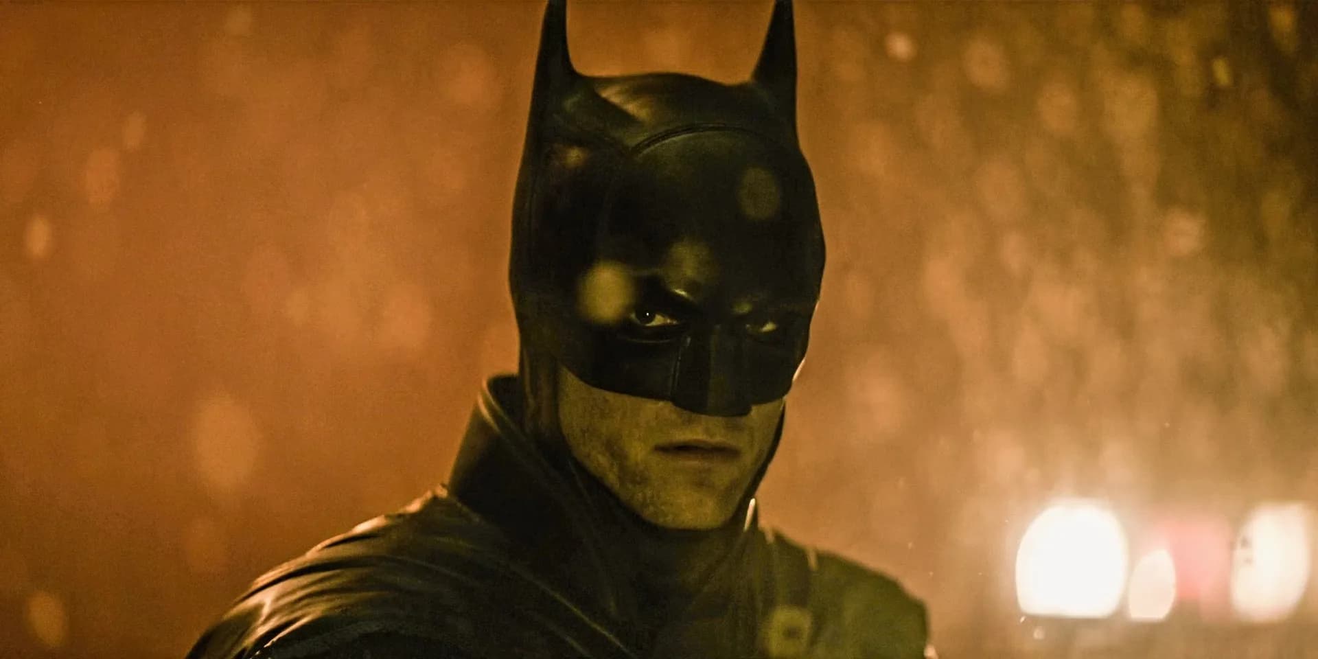 Robert Pattinson in a dark suit, face half-shadowed, standing in front of a Gotham skyline.