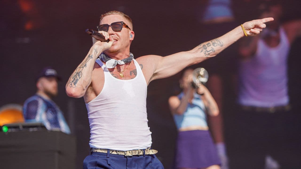 Macklemore performing on stage with a crowd in the background at a stadium concert
