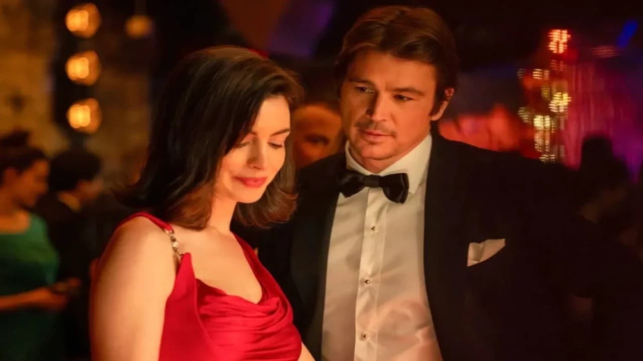 Anne Hathaway in a dark, high-collared dress, staring into the camera with a cold, knowing look.