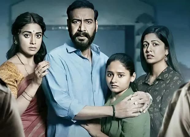 Ajay Devgn in a quiet, intense pose, eyes locked on the camera, in a dimly lit room.