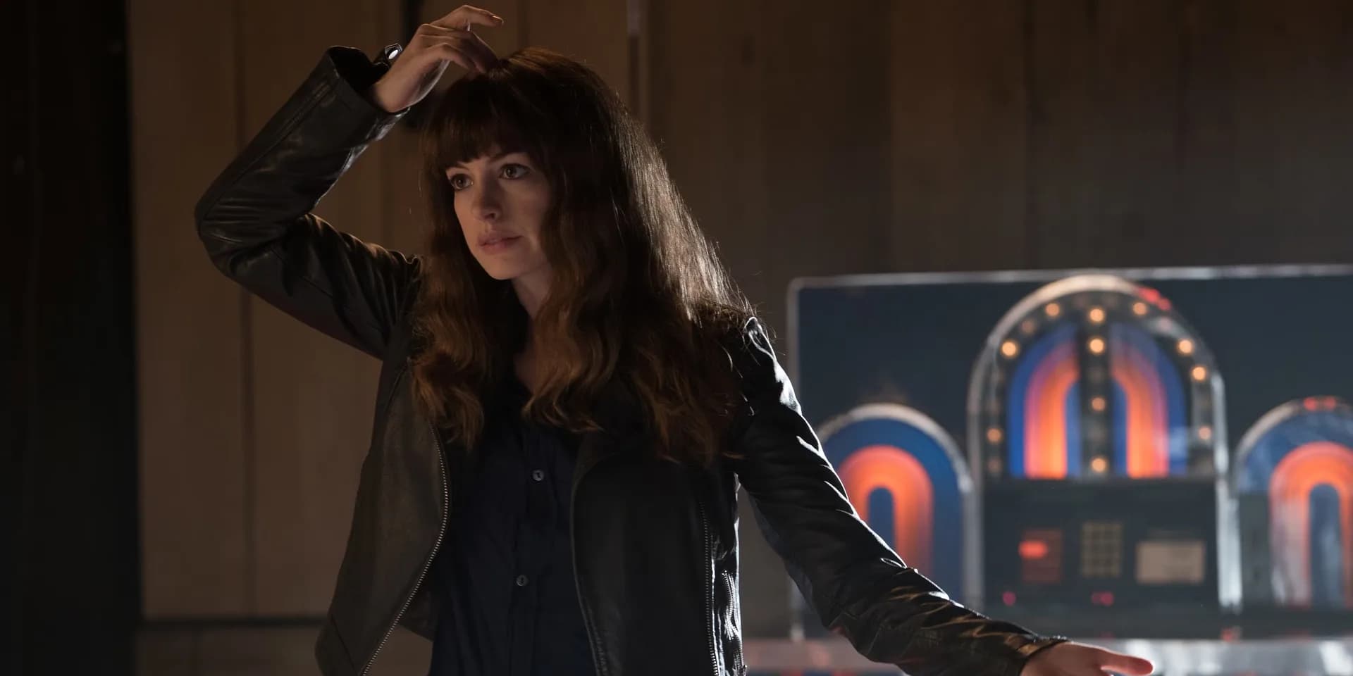 Anne Hathaway in a dramatic pose, standing in front of a city skyline being destroyed by a giant creature