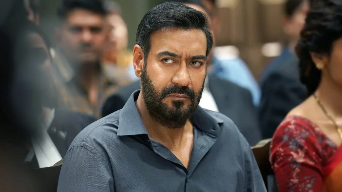 A still from Drishyam 3 showing Ajay Devgn in a tense expression, standing against a dark background.