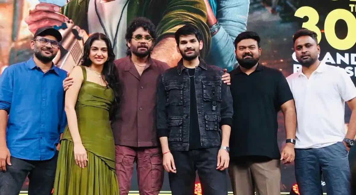 Nagarjuna at a press event, holding a film poster with Aniesh and Anaswara Rajan