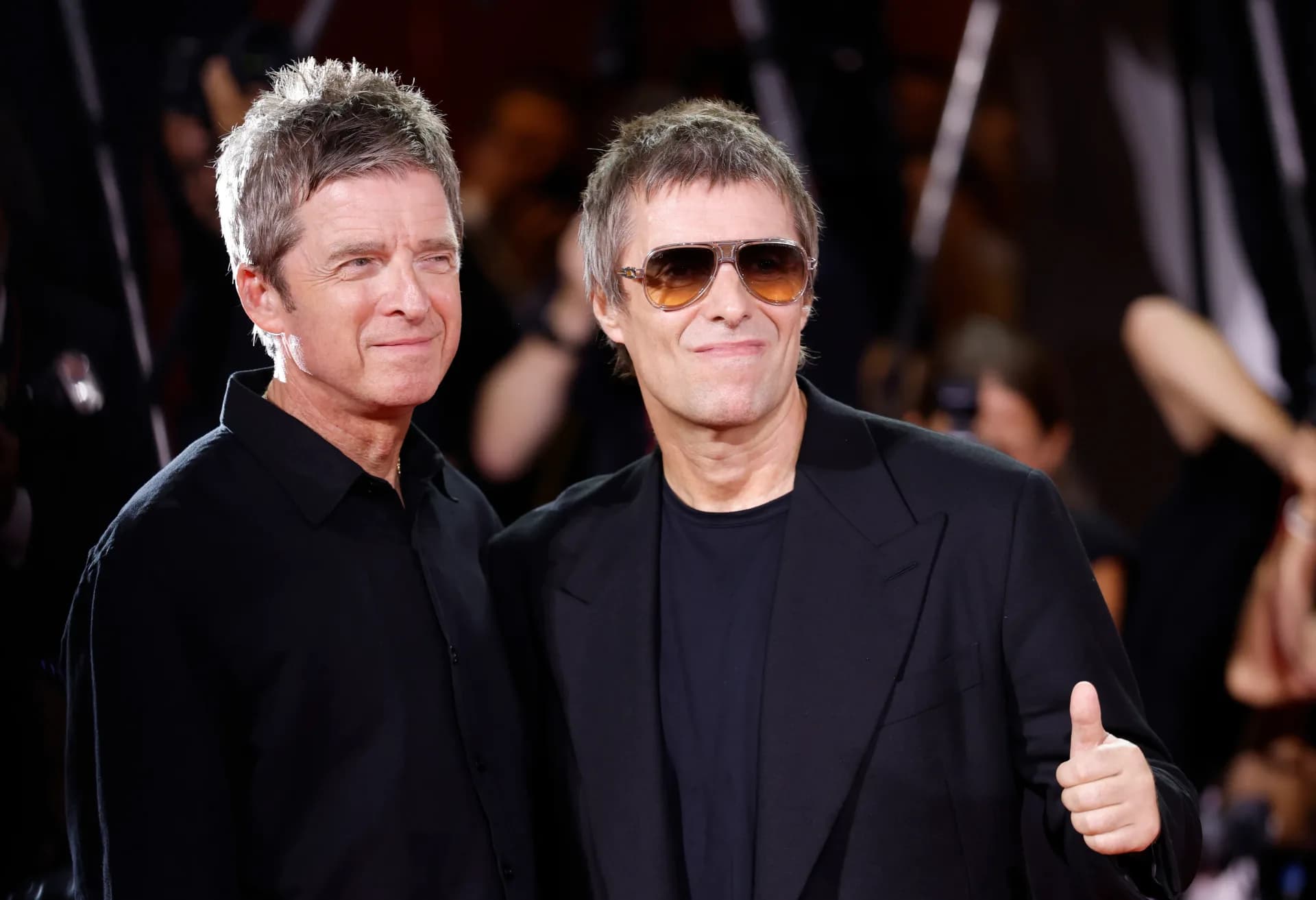 Liam and Noel Gallagher raising their joined fists on the red carpet at the Venice Film Festival premiere of their Oasis documentary.